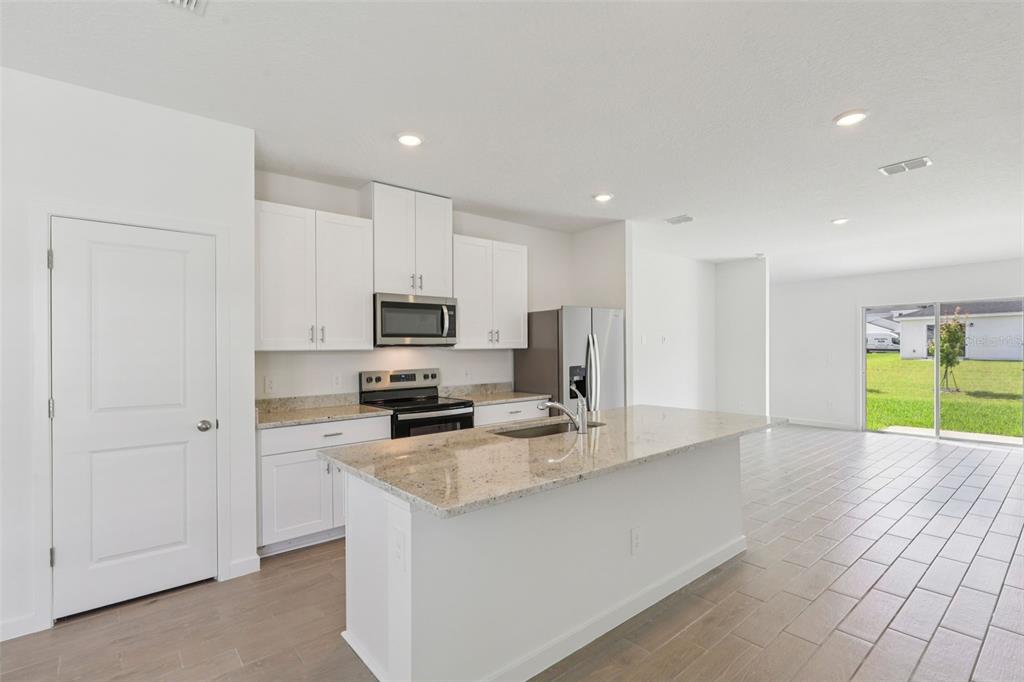 A modern kitchen features white cabinets, granite countertops, a center island, and tile flooring — 16 DERBYSHIRE DRIVE, PALM COAST, FL
