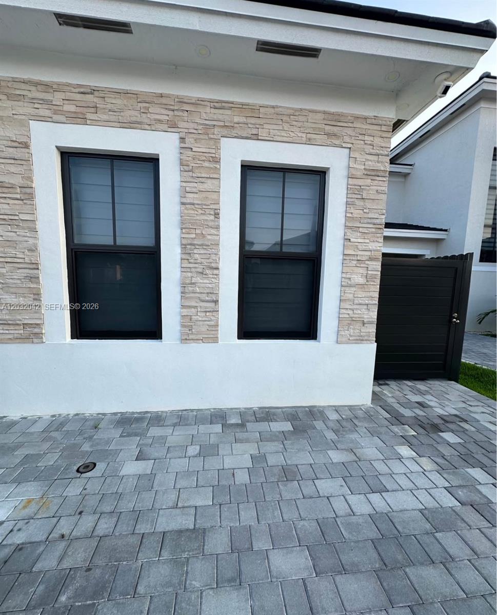 The exterior of a house features stone veneer walls, two dark-framed windows, and paver flooring — 14429 SW 19th St # 1, Miami FL 33175, MIAMI, FL