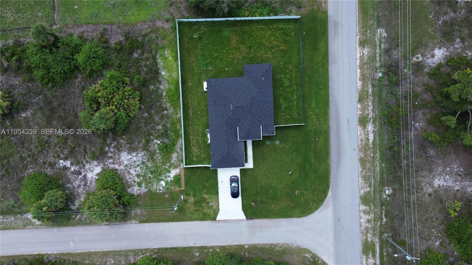 An aerial view shows a house with a dark roof on a fenced lot — 1111 GUNBY AVE S, Lehigh Acres FL 33974, LEHIGH ACRES, FL