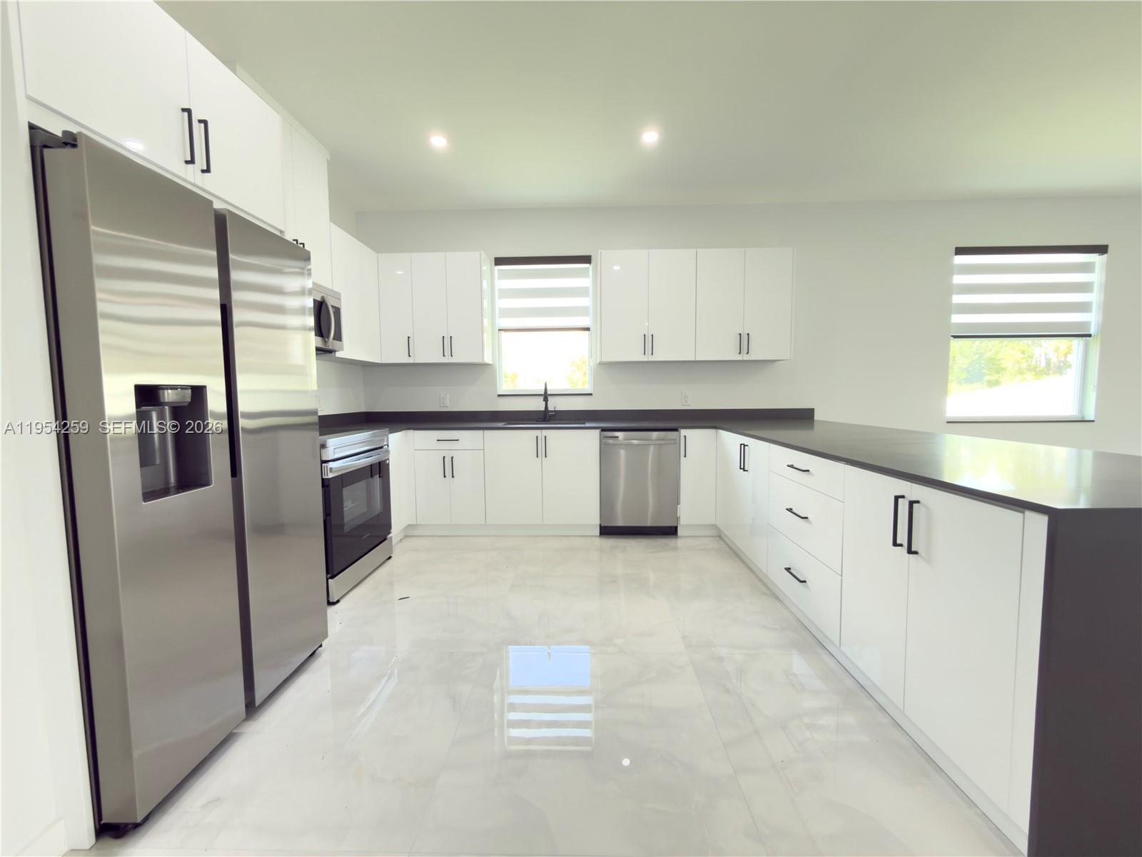 A modern kitchen features white cabinets, stainless steel appliances, and dark countertops on tile floors — 1111 GUNBY AVE S, Lehigh Acres FL 33974, LEHIGH ACRES, FL