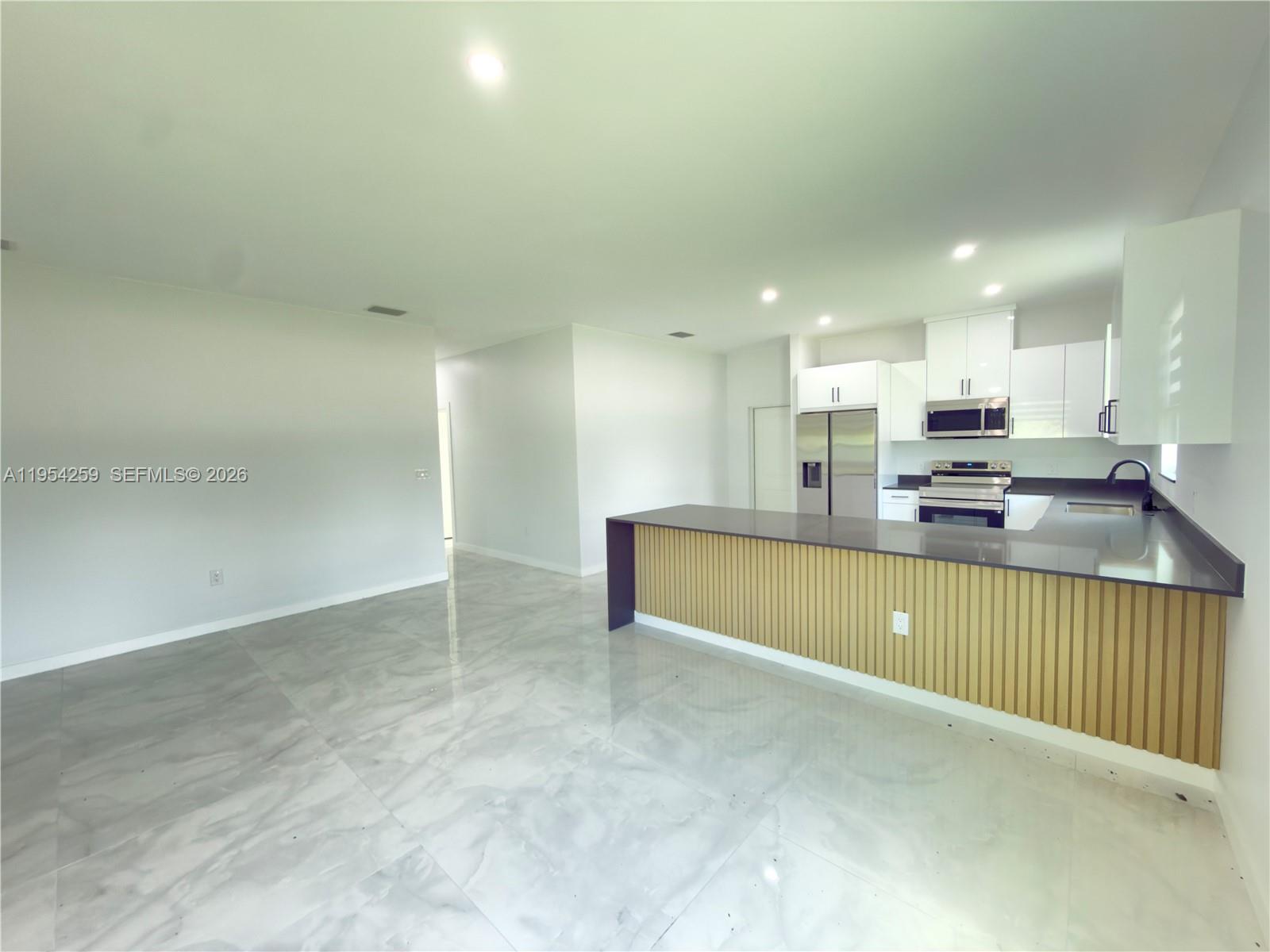 A modern kitchen features white cabinets, stainless steel appliances, and a slatted wood island base — 1111 GUNBY AVE S, Lehigh Acres FL 33974, LEHIGH ACRES, FL