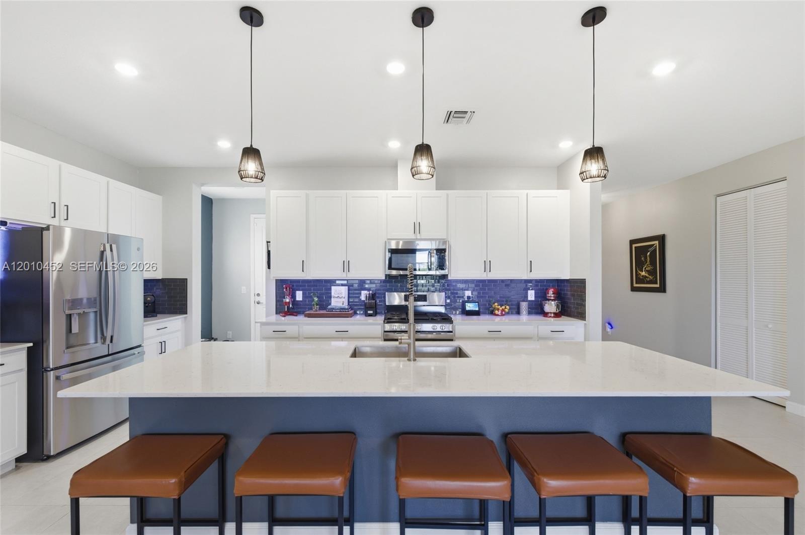 A modern kitchen features white cabinets, a blue tiled backsplash, and a large quartz island — 1902 Wandering Willow Way, Loxahatchee FL 33470, LOXAHATCHEE, FL