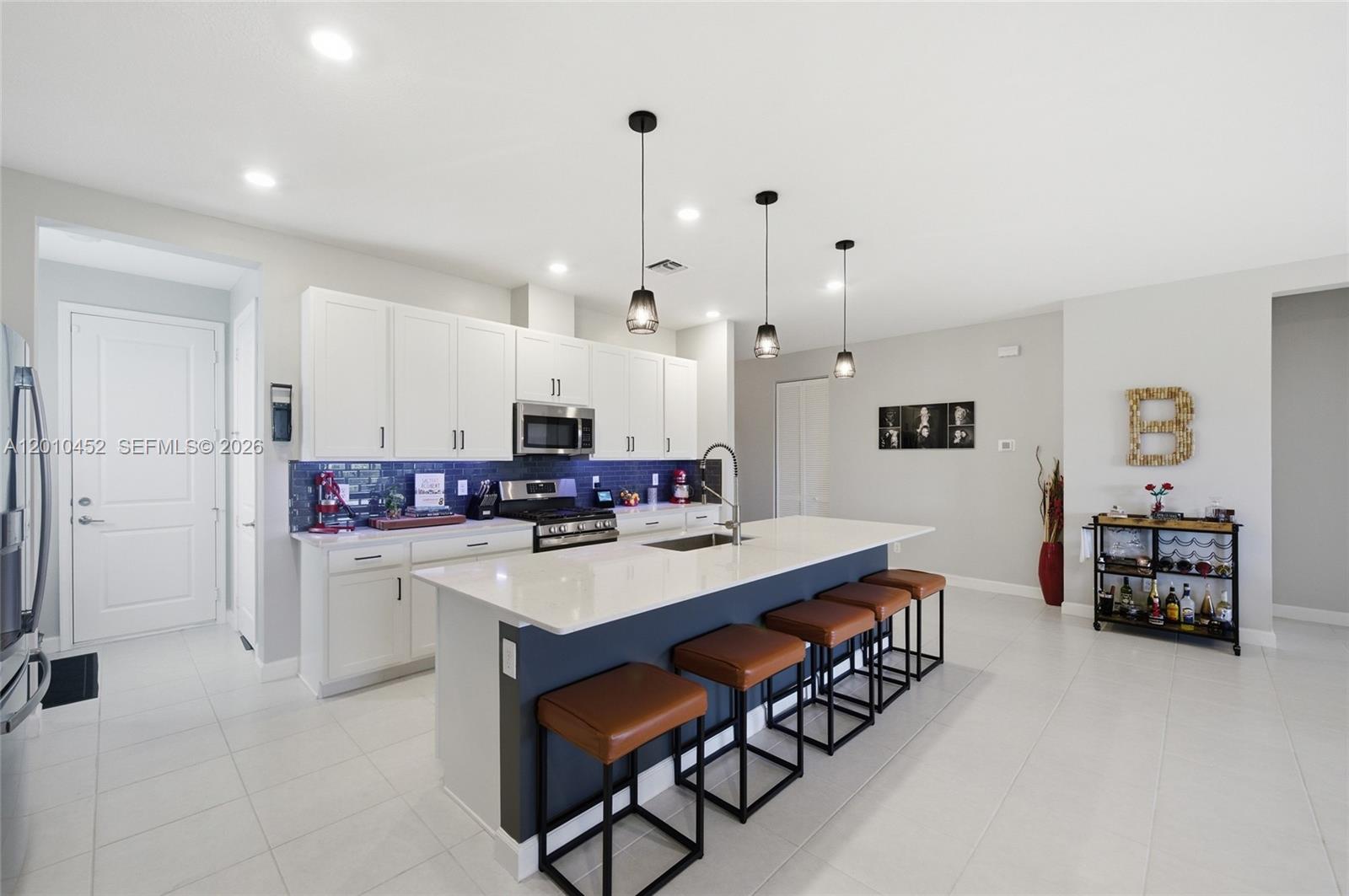 A modern kitchen features white cabinets, a dark blue island with bar stools, and tile flooring — 1902 Wandering Willow Way, Loxahatchee FL 33470, LOXAHATCHEE, FL