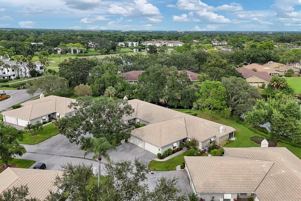 An aerial view shows several residential buildings with tan tile roofs surrounded by lush landscaping — 3244 RINGWOOD MEADOW UNIT 77, SARASOTA, FL