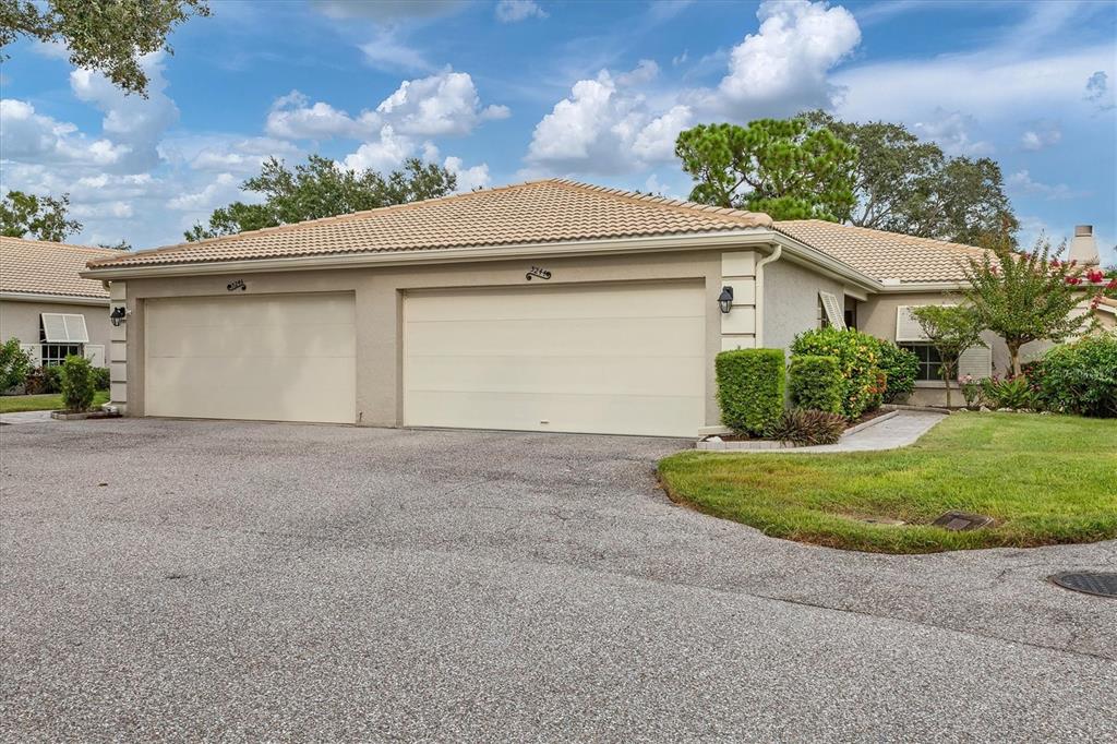 A tan duplex house with two garage doors and a tiled roof under a cloudy sky — 3244 RINGWOOD MEADOW UNIT 77, SARASOTA, FL
