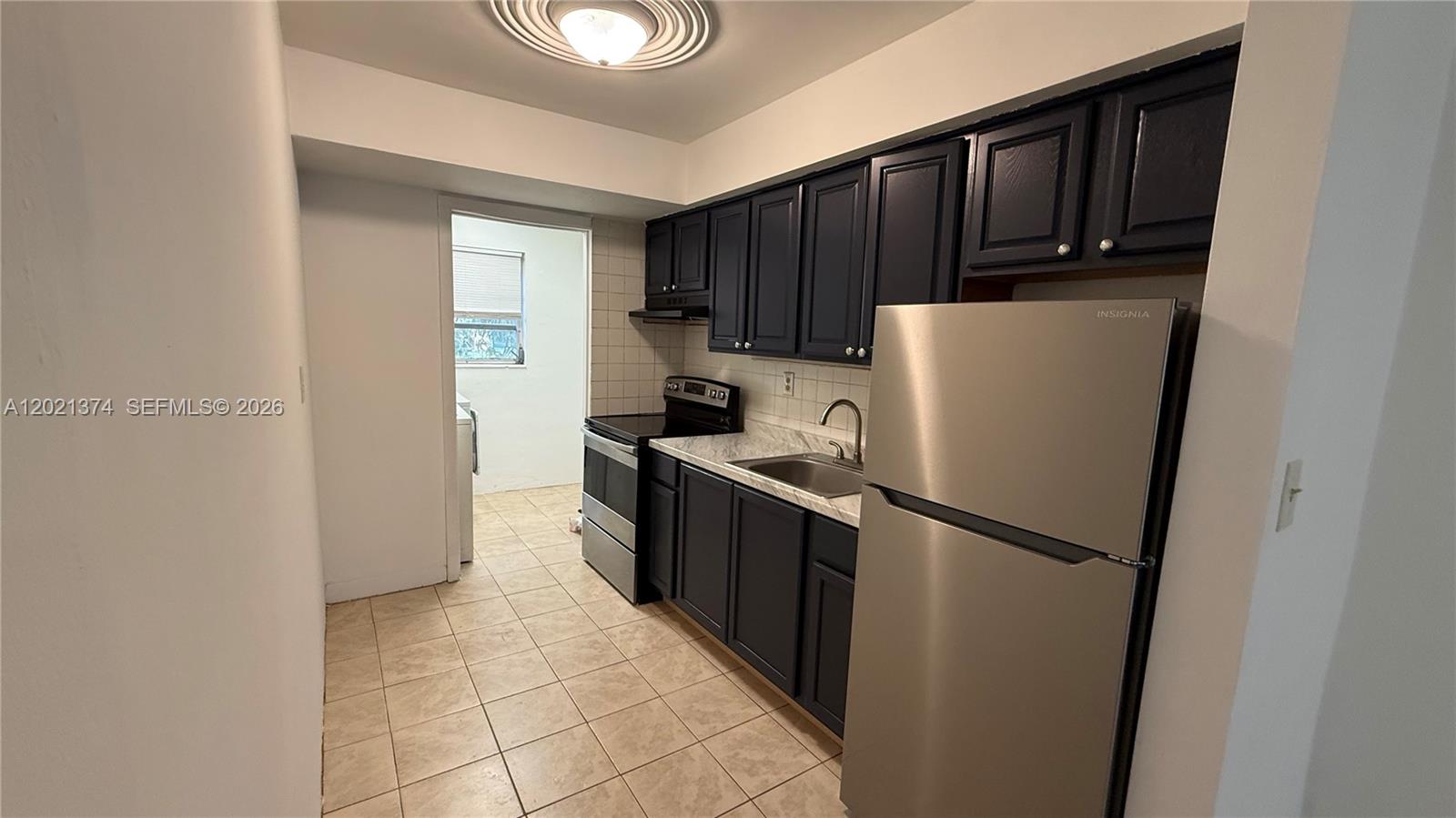 A kitchen features dark cabinets, stainless steel appliances, and light-colored tile flooring — 4940 SW 28th Ter, Dania Beach FL 33312, DANIA BEACH, FL