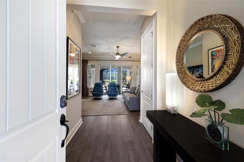 An entryway leads into a living room with wood-look tile floors and a round mirror — 4821 ROYAL DORNOCH CIRCLE, BRADENTON, FL