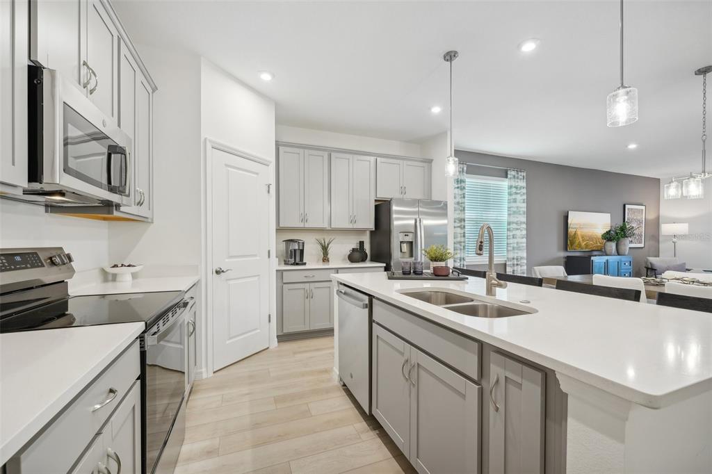 A modern kitchen features gray cabinets, white countertops, stainless steel appliances, and a central island — 12831 TROVITA DRIVE, GRAND ISLAND, FL