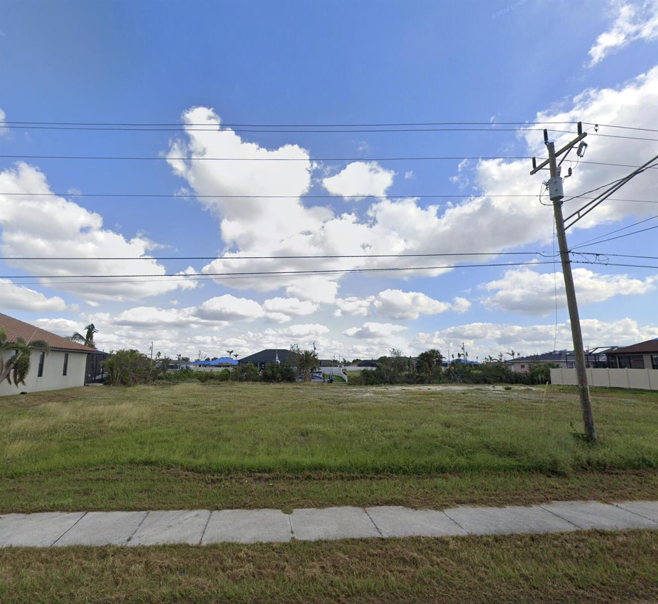 A vacant, grassy residential lot sits between two houses under a blue, cloudy sky — 2513 Surfside Boulevard, FL 33914, FL