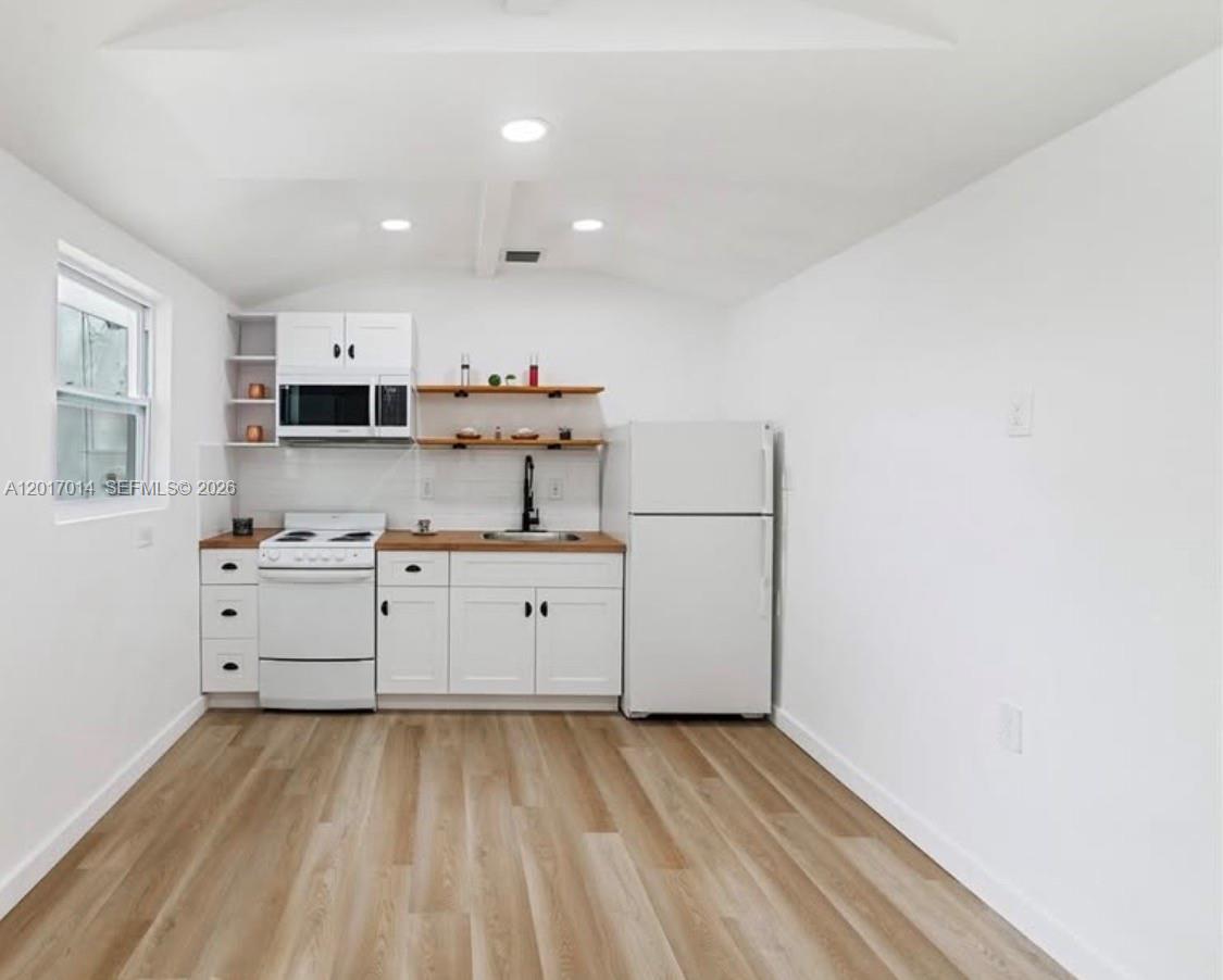 A small kitchen features white cabinets, a white stove, a refrigerator, and wood-look flooring — 954 NW 75th St # b, Miami FL 33150, MIAMI, FL
