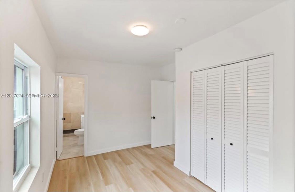A bedroom with light wood-look flooring, white walls, a closet with louvered doors, and an ensuite — 954 NW 75th St # b, Miami FL 33150, MIAMI, FL