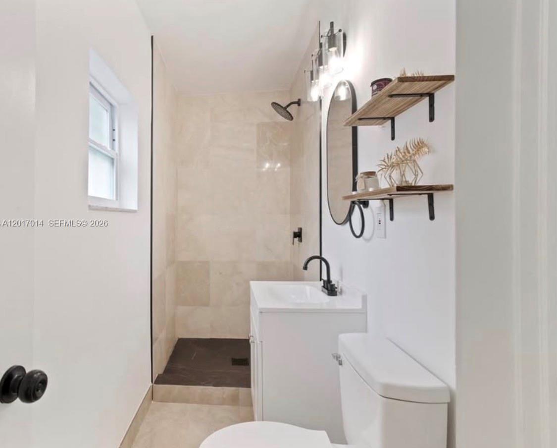 A small bathroom features a walk-in shower, a white vanity, and open wooden wall shelves — 954 NW 75th St # b, Miami FL 33150, MIAMI, FL