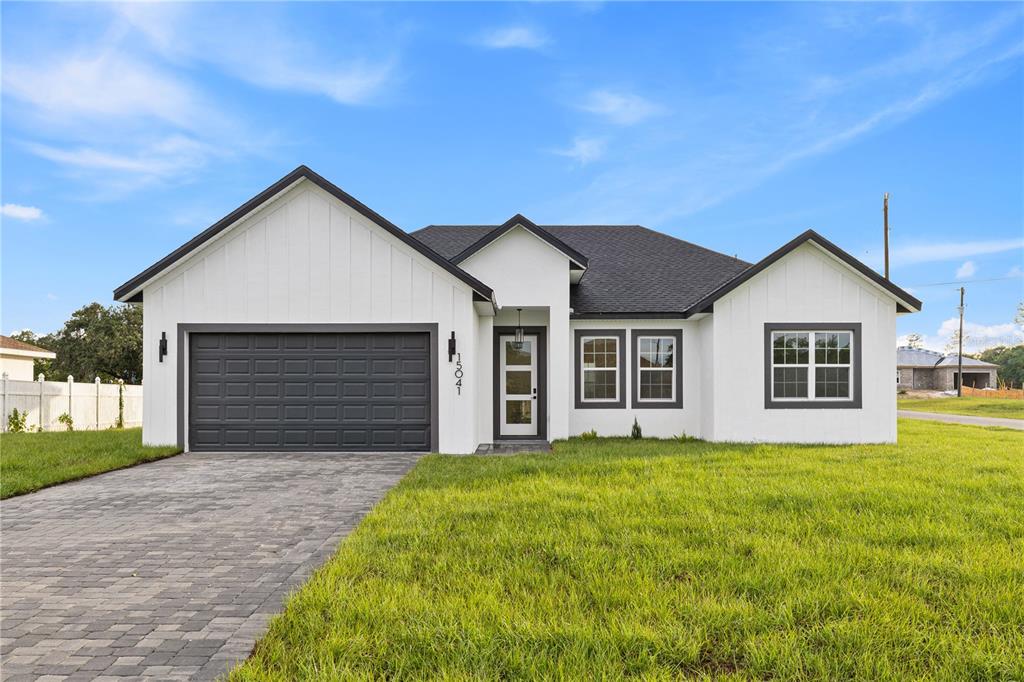 A single-story white house with board-and-batten siding, a dark roof, and a paved driveway — 15041 SW 24TH CIRCLE, OCALA, FL