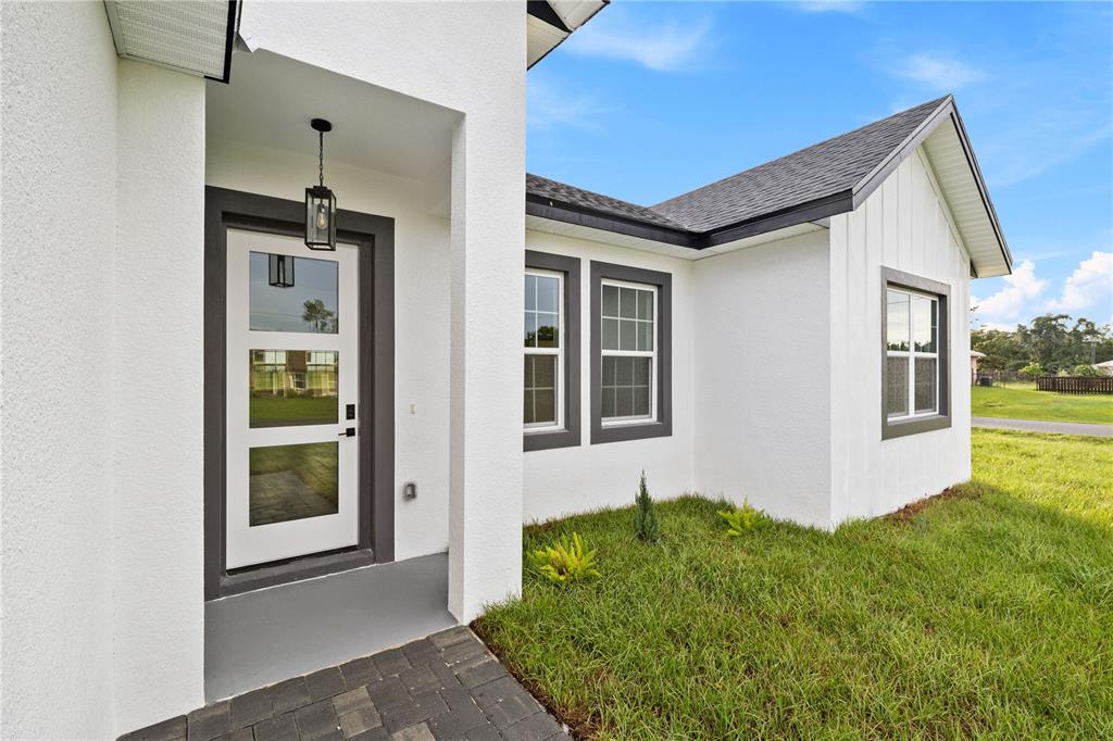 A white stucco house exterior features a modern front door, dark trim, and a walkway — 15041 SW 24TH CIRCLE, OCALA, FL