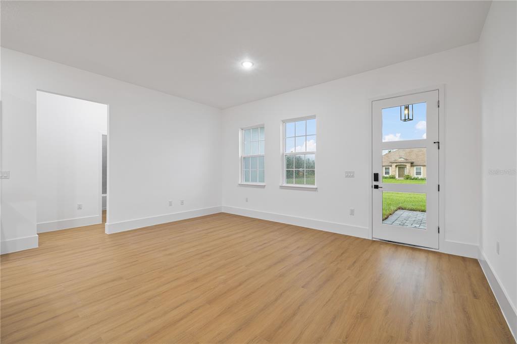 An empty room with light wood-look flooring, white walls, two windows, and a glass-paneled door — 15041 SW 24TH CIRCLE, OCALA, FL