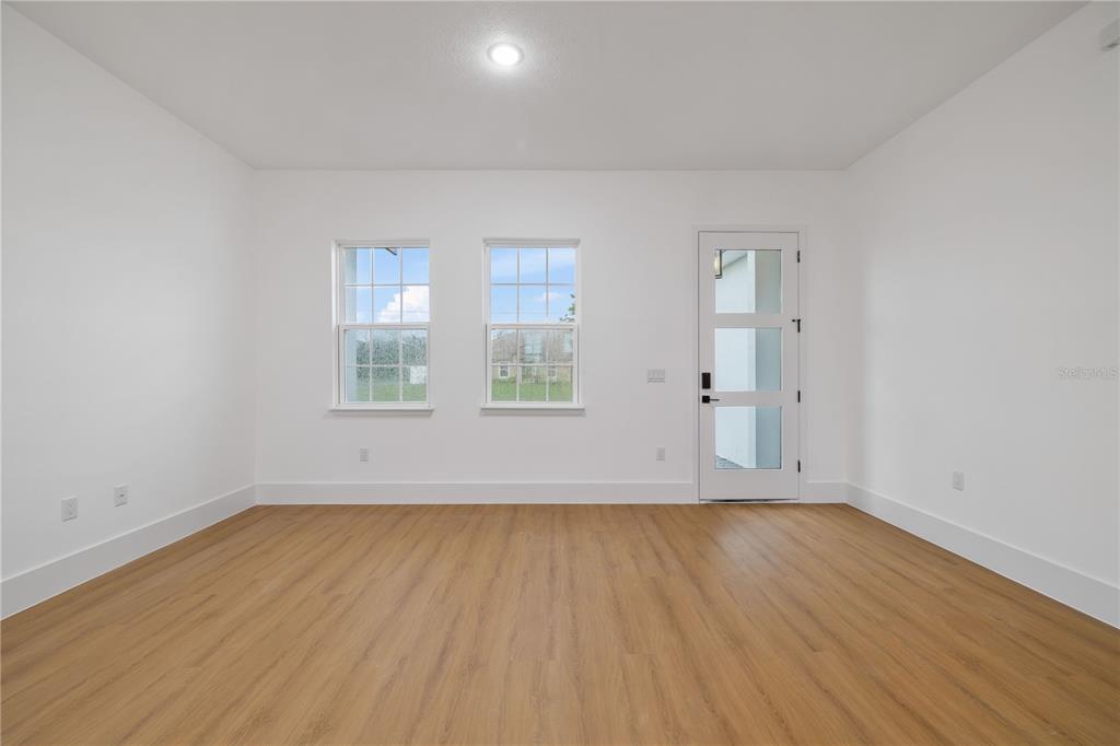 A bright, empty room features light wood-look flooring, white walls, two windows, and a glass-paneled door — 15041 SW 24TH CIRCLE, OCALA, FL