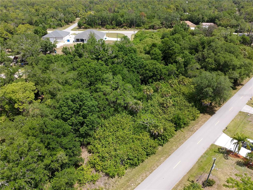 An aerial view shows a wooded, undeveloped lot situated between a paved road and houses — 1189 EPPINGER DRIVE, PORT CHARLOTTE, FL