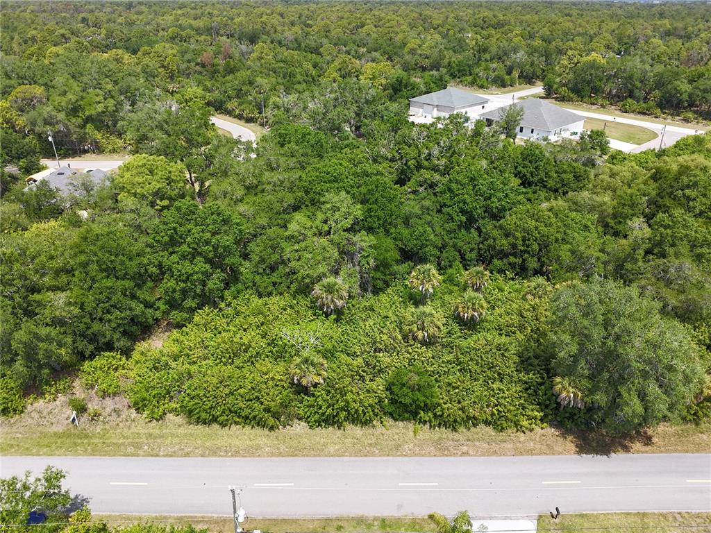 An aerial view shows a wooded, undeveloped lot situated along a paved road — 1189 EPPINGER DRIVE, PORT CHARLOTTE, FL