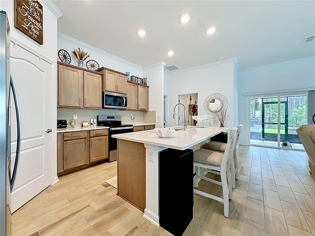 A kitchen features light wood cabinets, a white quartz island with seating, and tile flooring — 153 GREENWOOD DRIVE, PALM COAST, FL