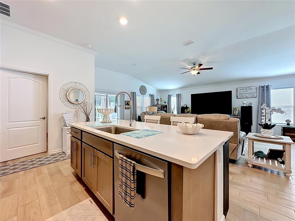 A kitchen island with a sink and stainless steel dishwasher overlooks a living room area — 153 GREENWOOD DRIVE, PALM COAST, FL