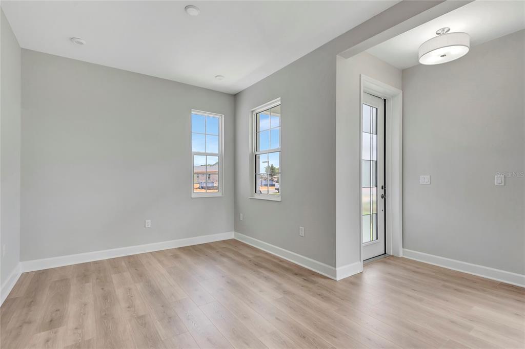 A bright room with light gray walls, wood-look flooring, two windows, and a glass door — 1459 SANTORINI WAY, TAVARES, FL
