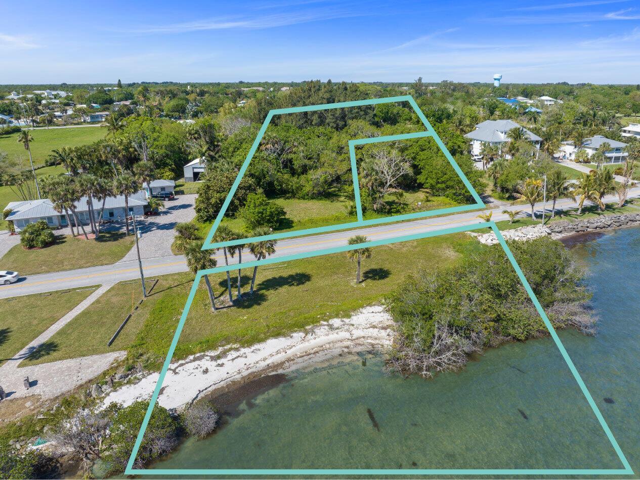 An aerial view shows two waterfront land parcels outlined in teal along a coastal road — SEBASTIAN, FL