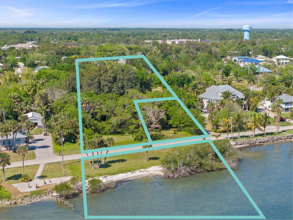 An aerial view shows a waterfront property with a large wooded lot and shoreline — SEBASTIAN, FL