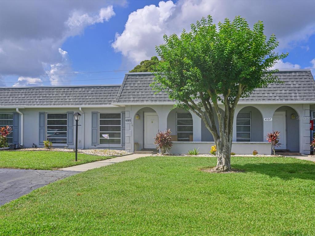 A single-story duplex with gray siding, arched entryways, and a large tree in the yard — 4105 35TH AVENUE W UNIT 4105, BRADENTON, FL