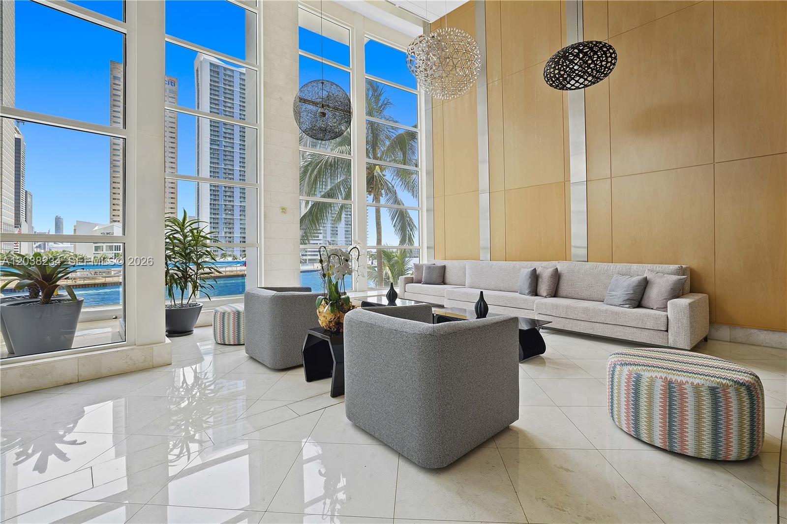 A modern, high-ceilinged lobby features floor-to-ceiling windows, grey furniture, and light-colored tile flooring — 901 Brickell Key Blvd # 2408, Miami FL 33131, MIAMI, FL