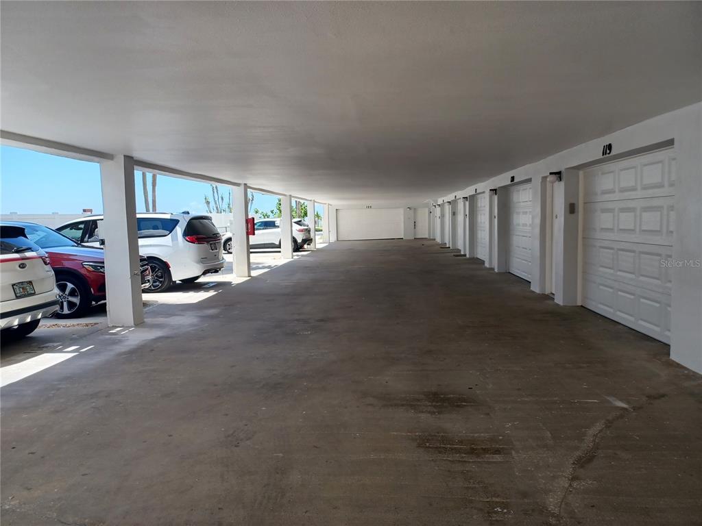 A covered parking area features a concrete floor, support pillars, and multiple garage doors — 17960 GULF BOULEVARD UNIT 118, REDINGTON SHORES, FL