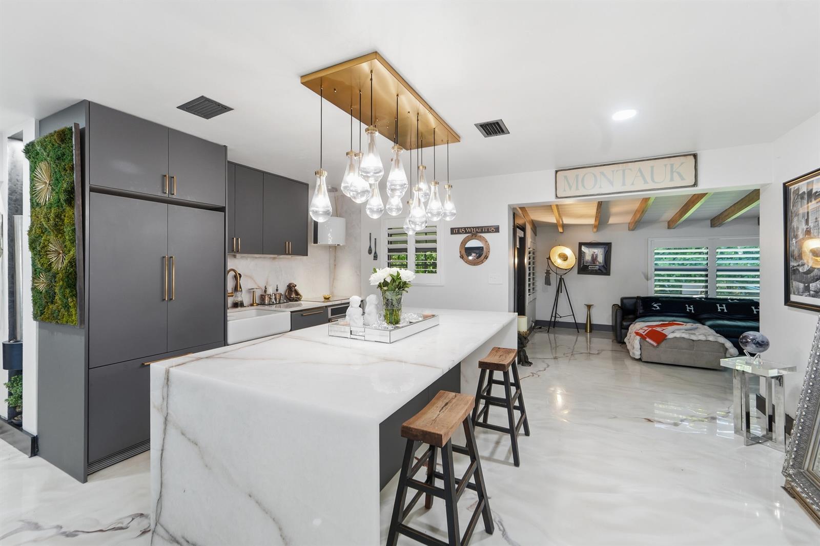 A modern kitchen features a large marble waterfall island, dark cabinetry, and a gold pendant light — 722 Greenbriar Drive, Lake Park FL 33403, LAKE PARK, FL