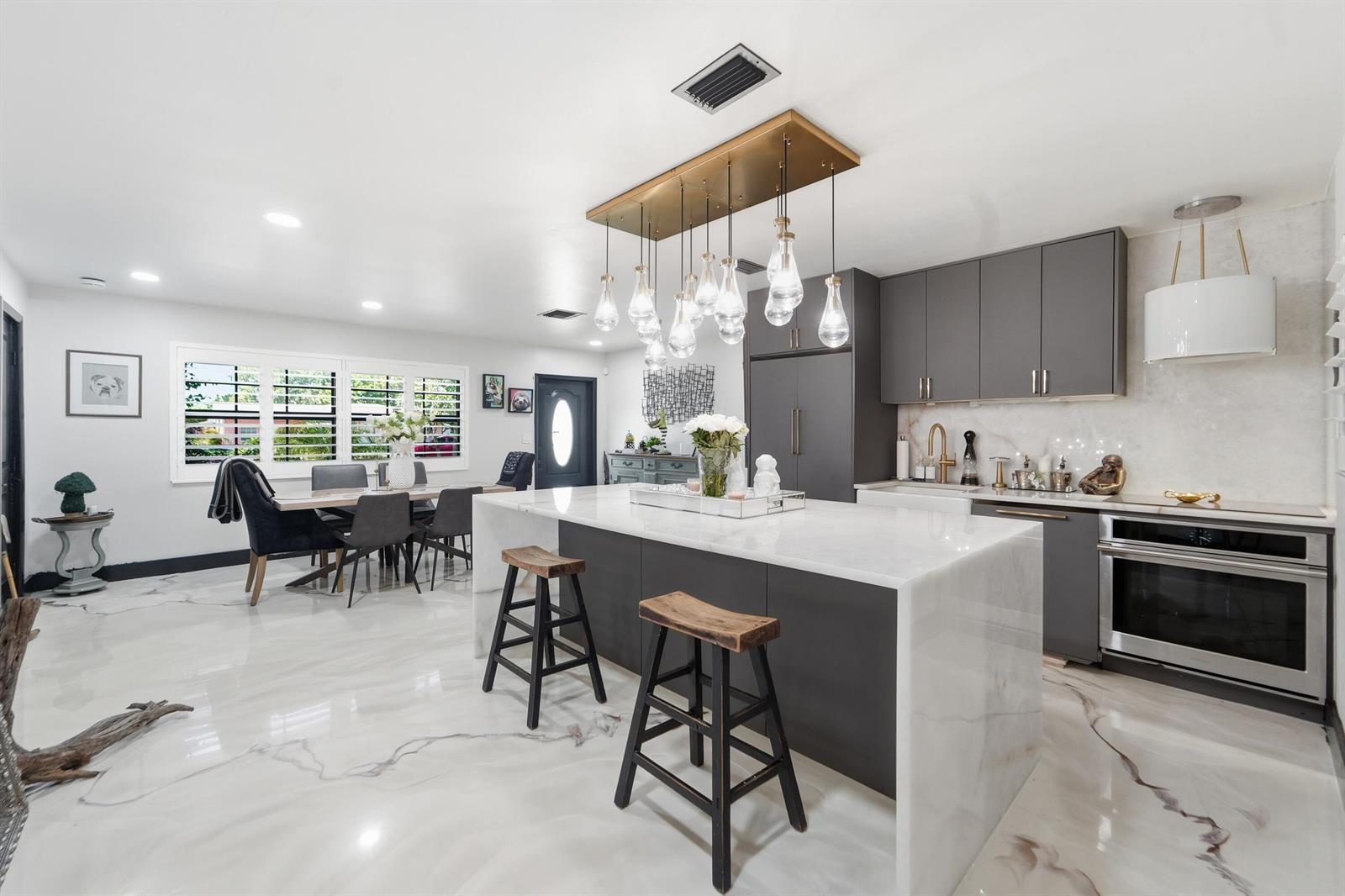 A modern kitchen features a large marble waterfall island, gray cabinetry, and glossy marble flooring — 722 Greenbriar Drive, Lake Park FL 33403, LAKE PARK, FL