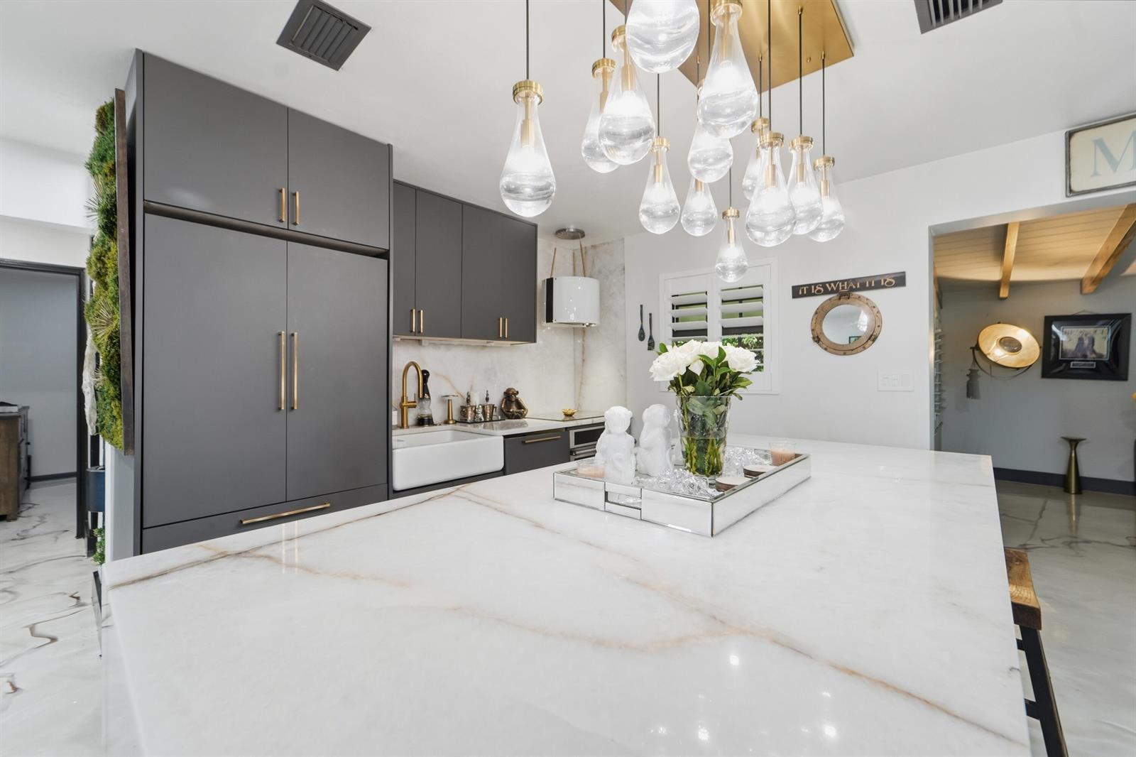 A modern kitchen features a large marble island, dark gray cabinetry, and a tiered glass chandelier — 722 Greenbriar Drive, Lake Park FL 33403, LAKE PARK, FL