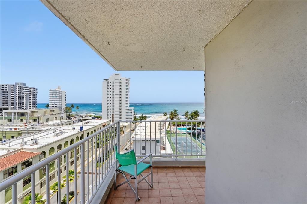 A balcony with a tiled floor, metal railing, and a folding chair overlooks the ocean — 1477 Ave Ashford TORRE DEL MAR UNIT 801, SAN JUAN, PR