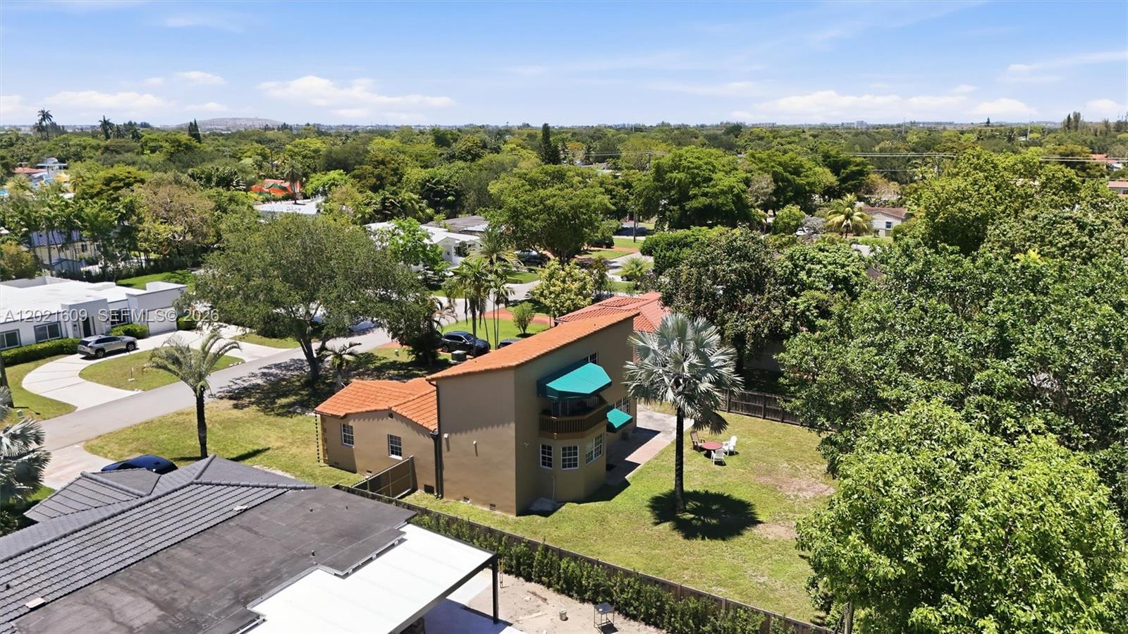An aerial view shows a two-story tan house with a red tile roof and green awnings — 245 Lenape Dr, Miami Springs FL 33166, MIAMI SPRINGS, FL