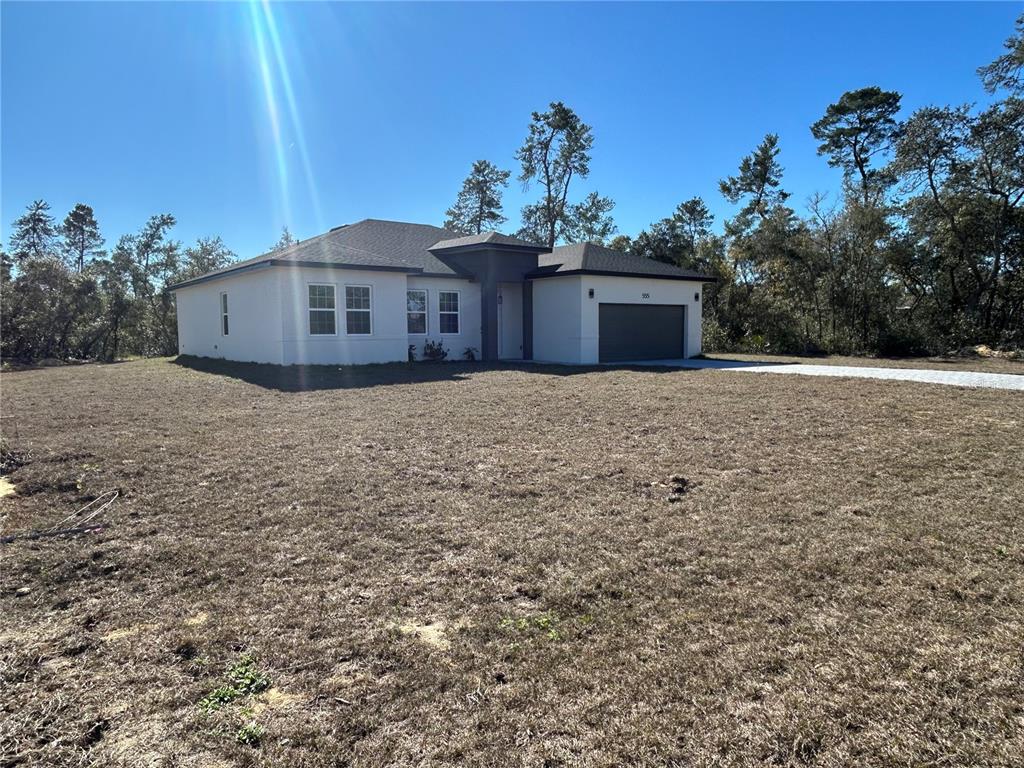 A single-story white house with a dark garage and roof sits on a grassy lot — 555 MARION OAKS GOLF ROAD, OCALA, FL