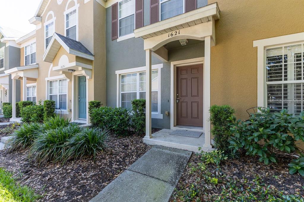 The exterior of a two-story townhouse features a brown front door and a concrete walkway — 1621 STOCKTON DRIVE, SANFORD, FL