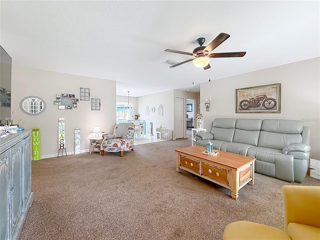 A living room features beige walls, brown carpeting, a light-colored sofa, and a ceiling fan — 6050 SW 155TH STREET ROAD, OCALA, FL