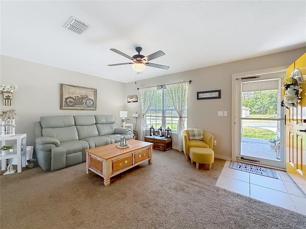 A living room features a grey sofa, a wooden coffee table, and a yellow armchair — 6050 SW 155TH STREET ROAD, OCALA, FL