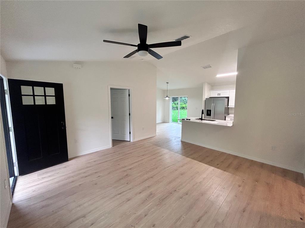 An open-concept living area features light wood-look flooring, a black front door, and a kitchen — 11491 NW 92ND CT, CHIEFLAND, FL