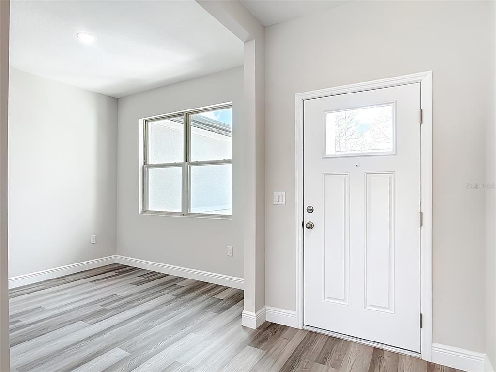 A room with light gray walls, wood-look flooring, a large window, and a white door — 2021 S CHAMBERLAIN BOULEVARD, NORTH PORT, FL