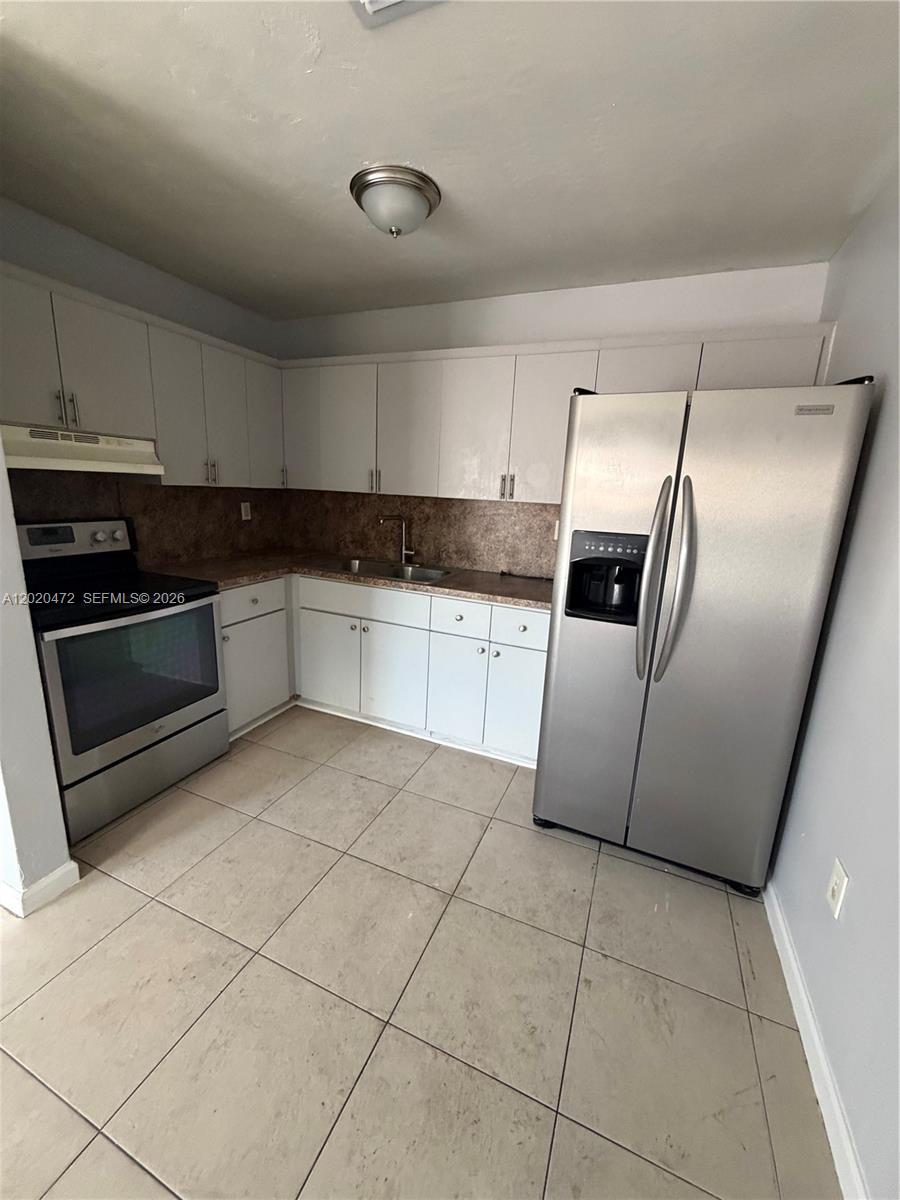 A kitchen features white cabinets, stainless steel appliances, a brown backsplash, and tiled flooring — 2924 NW 132nd Ter # 3, Opa-Locka FL 33054, OPA-LOCKA, FL