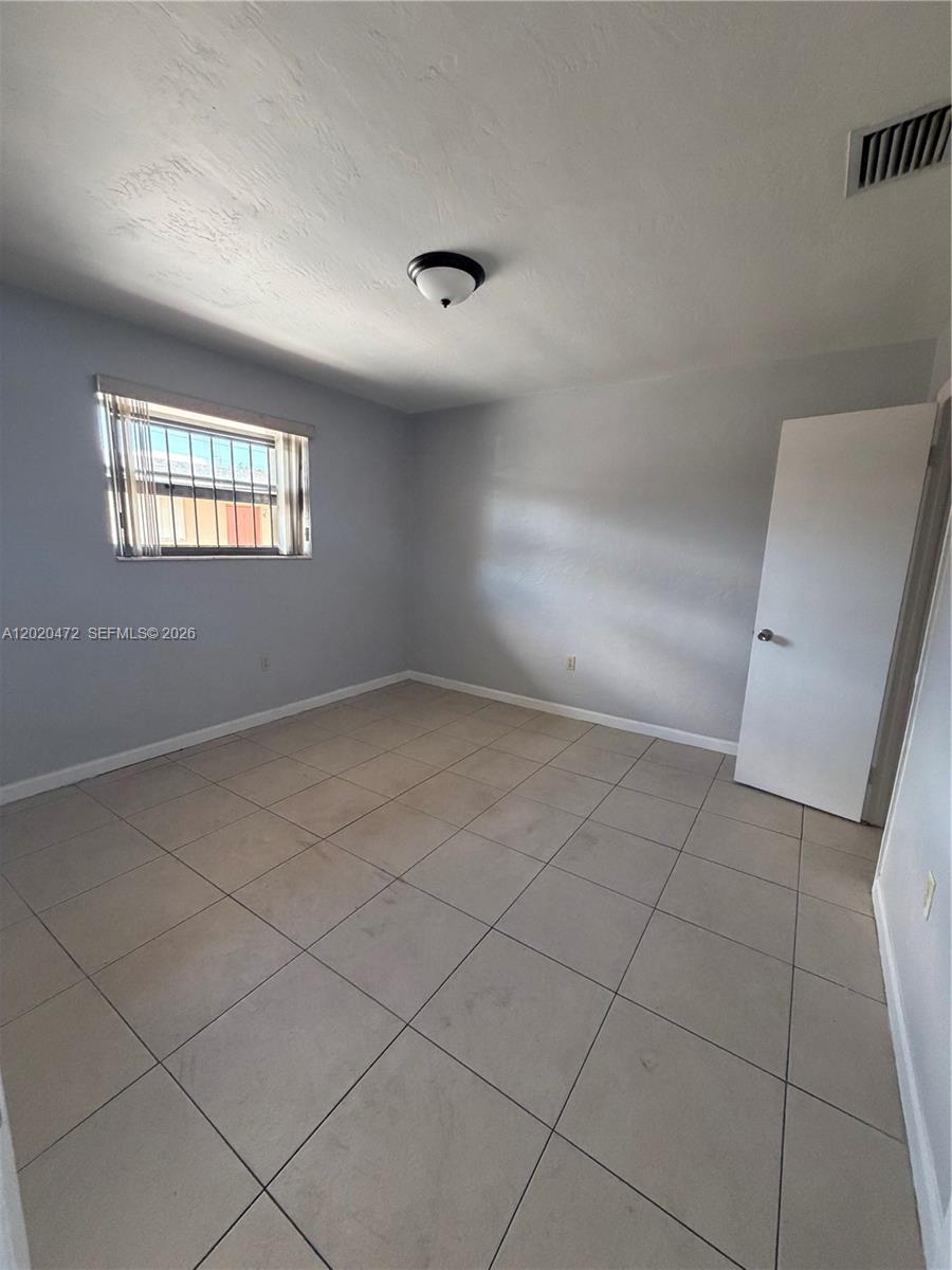 A bedroom with light gray walls, beige tile flooring, a window with security bars, and a door — 2924 NW 132nd Ter # 3, Opa-Locka FL 33054, OPA-LOCKA, FL
