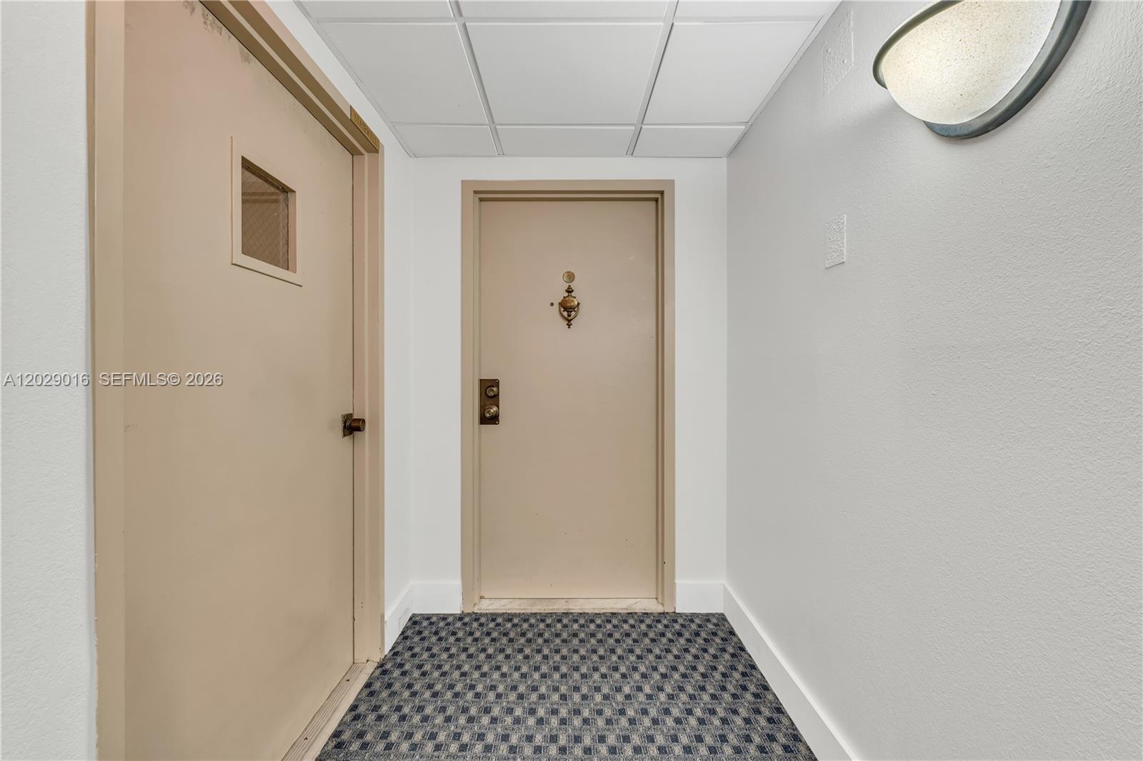 A hallway features two beige doors, a patterned carpet, and a wall-mounted light fixture — 1450 Brickell Bay Dr # 1815, Miami FL 33131, MIAMI, FL