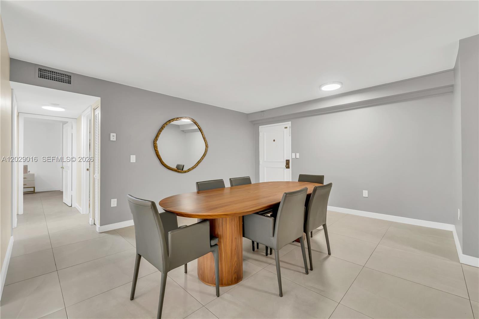 A dining room features a wooden oval table, six gray chairs, and a round mirror — 1450 Brickell Bay Dr # 1815, Miami FL 33131, MIAMI, FL