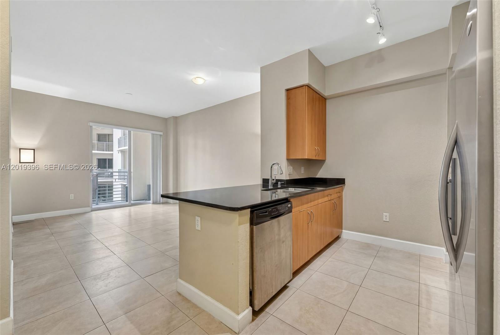 A kitchen with light wood cabinets, black countertops, and a dishwasher opens to a living area — 1830 Radius Dr # 1116, Hollywood FL 33020, HOLLYWOOD, FL