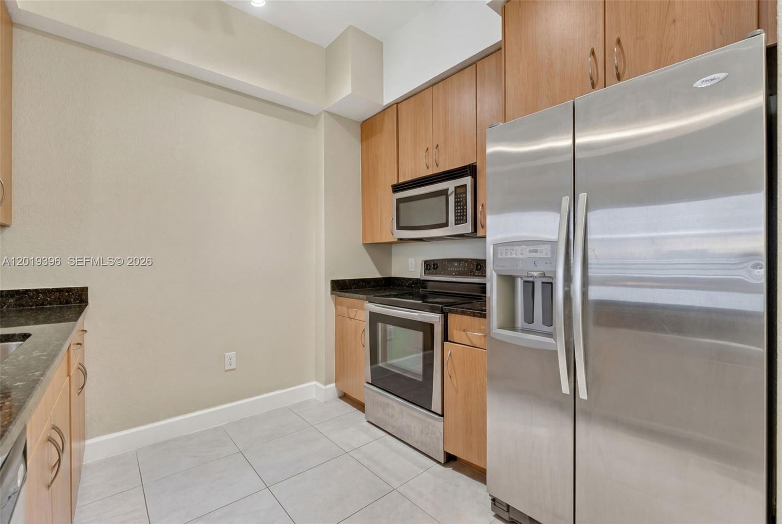 A kitchen features light wood cabinets, stainless steel appliances, and dark countertops — 1830 Radius Dr # 1116, Hollywood FL 33020, HOLLYWOOD, FL
