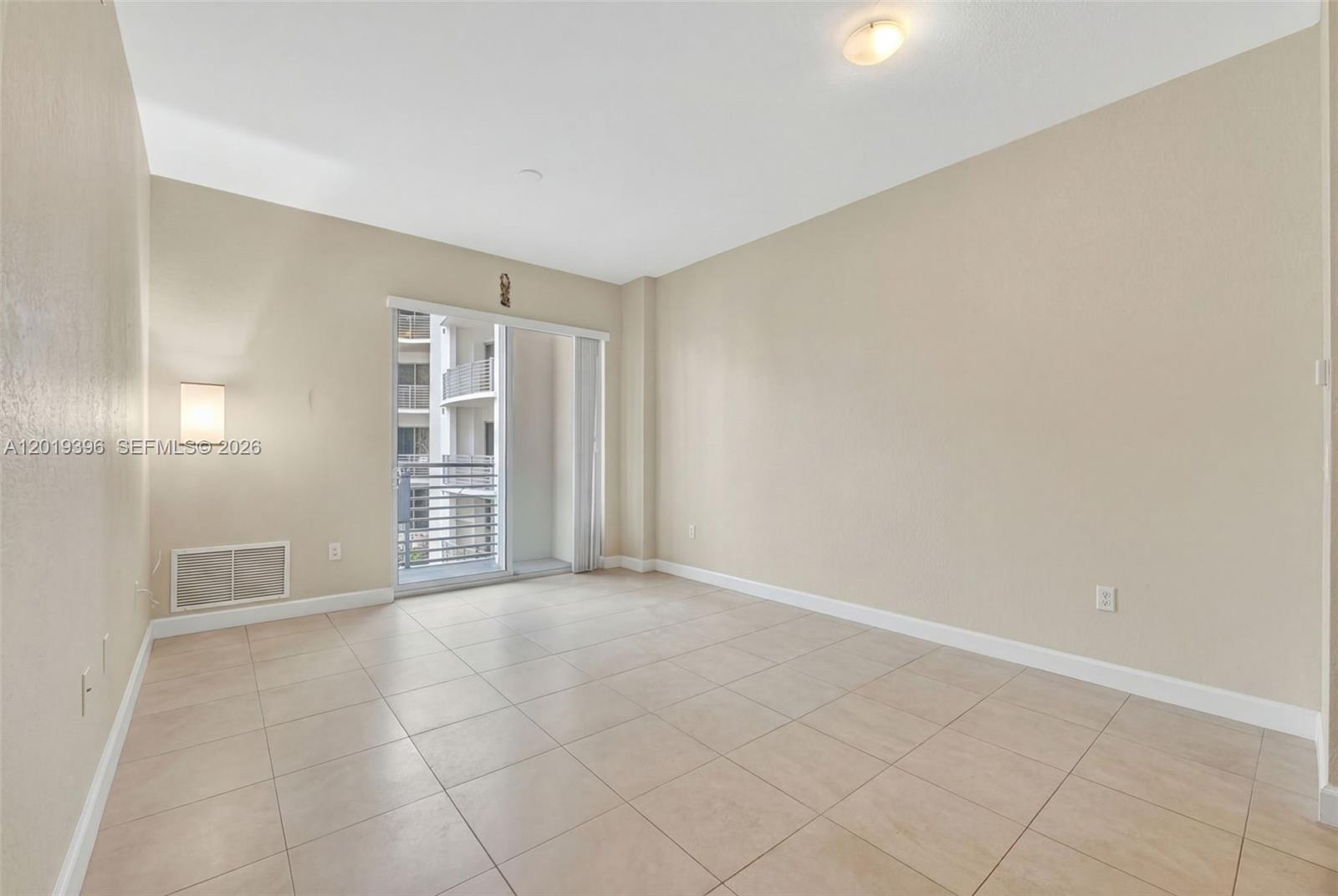 An empty room features beige walls, light-colored tile flooring, a ceiling light, and a balcony door — 1830 Radius Dr # 1116, Hollywood FL 33020, HOLLYWOOD, FL
