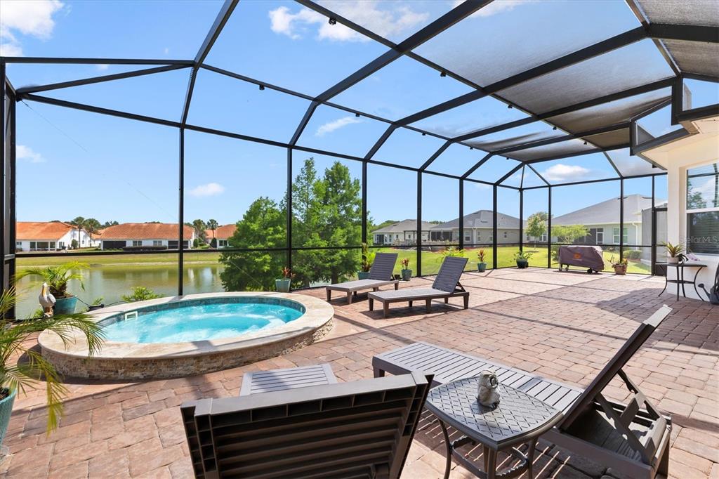 A screened-in patio features a circular hot tub, brick pavers, and views of a lake — 5105 JAREDS LANDING WAY, OXFORD, FL