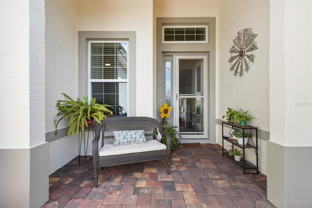 A covered front porch features a wicker bench, potted plants, and decorative wall art — 5105 JAREDS LANDING WAY, OXFORD, FL